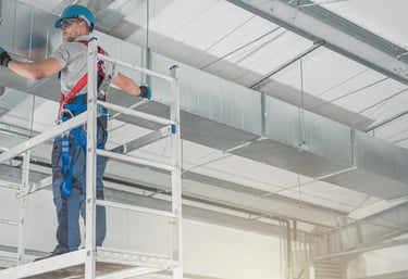 a man in a blue workwear suit and a helmet on a platform installing HVAC