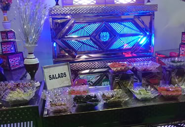 Buffet setup with assorted salads in glass bowls, a 'SALADS' sign, blue and purple lighting.