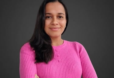 Professional woman in a pink ribbed sweater posing with arms crossed against a dark background.
