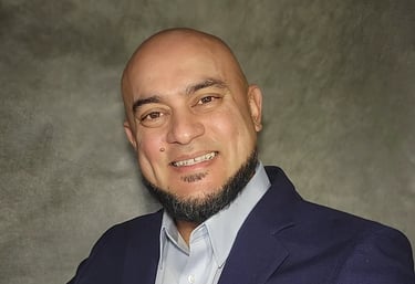 Professional headshot of a smiling bald man with a beard wearing a navy blue blazer and light blue shirt.