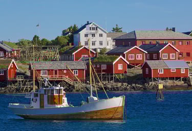 Traditional fishing boat docked in Reine harbor surrounded by red rorbuer cabins in Lofoten