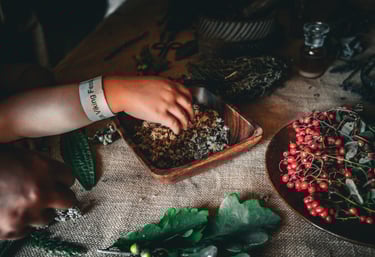 a child's hand taking herbs out of a wooden bowl beside a bowl of berries