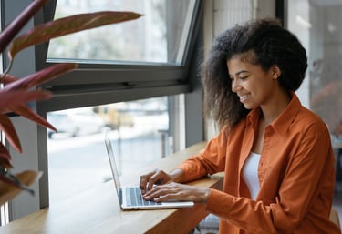 Smiling woman working on a laptop by a window, representing career growth, focus, and momentum