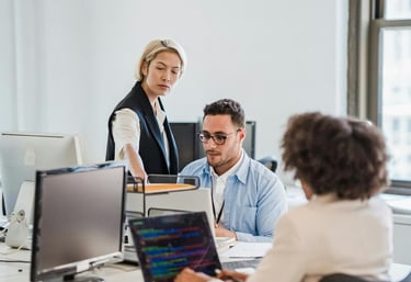 um homem e uma mulher sentados em uma mesa em um escritório movimentado