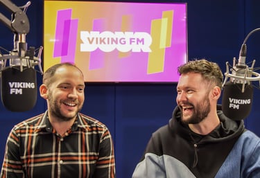 Alex Duffy and Calum Scott sit behind microphones in the Viking FM radio studio. Both are laughing.