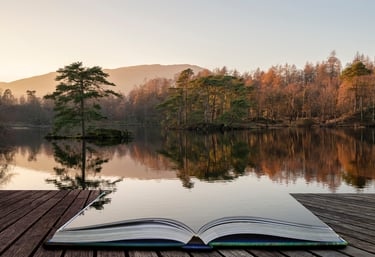Ein aufgeschlagenes Buch liegt auf einem Steg vor der Kulisse eines Sees mit bäumen in herbstlichen Farben.