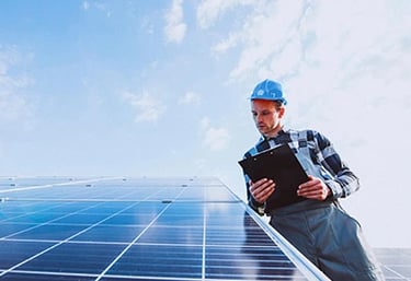 A solar technician in a hard hat inspects a residential photovoltaic panel system with a clipboard.