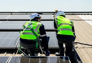 Two technicians in safety gear and hard hats installing solar panels on a rooftop for renewable energy.