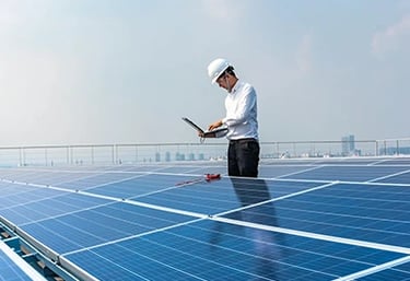 Engineer in a hard hat inspecting solar panels on a rooftop with a laptop for renewable energy maintenance.