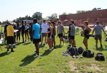 Group of track and field athletes gathered outdoors during a ThrowersClub meet, preparing for events
