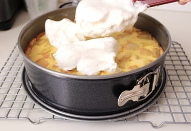 Spreading fluffy white meringue topping onto a freshly baked fruit tart in a springform pan.