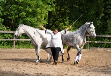 a woman in white shirt and black pants standing next to two white horses