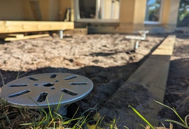 Adjustable steel screw piles installed in dirt for a backyard deck construction project.