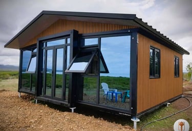 Modern prefab container home with wood cladding and large reflective glass windows in a rural landscape.