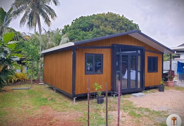 Modern wooden prefab tiny home with black trim nestled in a tropical garden landscape.