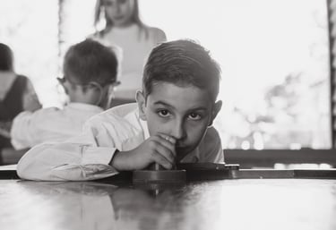 a boy is sitting at a table with his hands on his chin