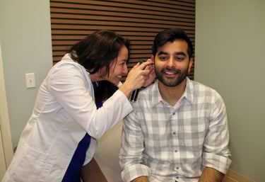 Dr Connolly uses an otoscope to perform an ear exam on a male patient in a clinic.