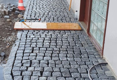 Natursteinplatten werden im Eingangsbereich verlegt – Werkzeuge und Holzplanke zeigen aktive Baustel