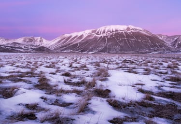 Piana di Castelluccio innevata con tramonto roseo e monti sullo sfondo