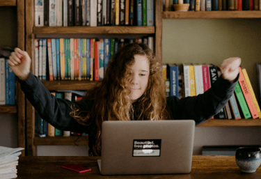 Young Gil with arms raised in celebration at a laptop