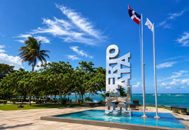 Puerto Plata sign and Dominican Republic flag at a tropical oceanfront park.