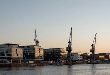 A wide photography shot of the Bristol harbor at golden hour, showing modern developments and historical cranes against a soft light grey and blue sky.