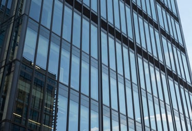 A modern North American / US office building with glass windows reflecting a clear sky blue sky. The image represents the innovative and solid foundation of our company.