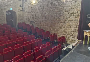 Intérieur d’un petit théâtre à l’ambiance intimiste, avec des rangées de fauteuils rouges face à une