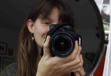 Caro hält eine Kamera und fotografiert sich im Spiegel. Ein persönlicher Einblick hinter die Kulisse