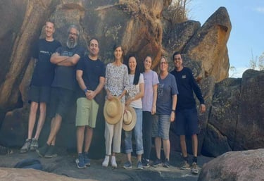 a group of people standing in front of a large rock formation - going out for bush walk