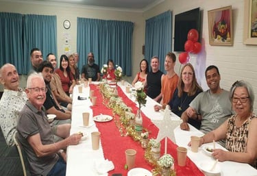 a group of people sitting at a long table - celebrating Christmas