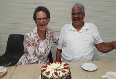 Two older adults laughing together at a table with a decorated cake.