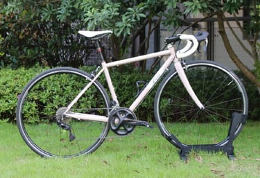A retro pink road bike with white drop handlebars parked on a green grass lawn.
