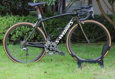 A black Specialized S-Works Venge carbon fiber road bike with tan wall tires parked on a green lawn.