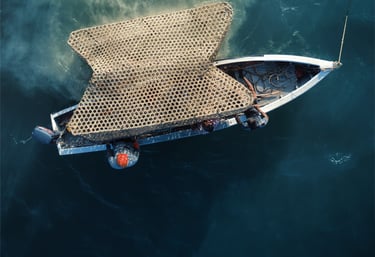 Aerial view of a fishing boat at sea carrying large, stacked bamboo traps on deep blue water.