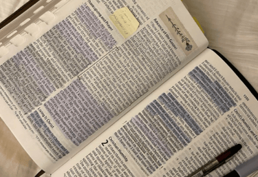 An open bible with highlighted scriptures with pens on a white linen sheet.