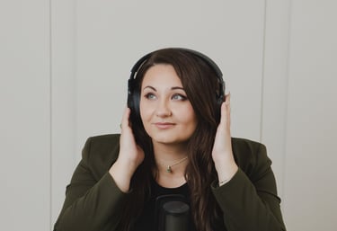 Adriana wearing headphones sits at a desk with a professional microphone recording a podcast.