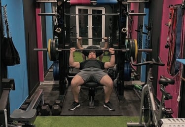 A client performing a barbell bench press in Robb Sheridans gym with a power rack and weights.