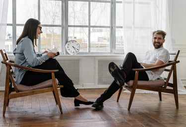 A woman and a man sat across from each other in a counselling setting, both are smiling