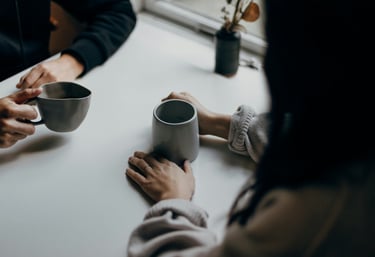 a therapist and client sit at a table, drinking coffee, having a private and empowering conversation