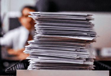 Una pila alta de documentos aprobados en una bandeja etiquetada como ACEPTADO