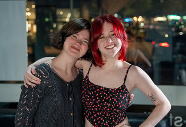 Two smiling young women with short hair and dyed red hair posing together at night.