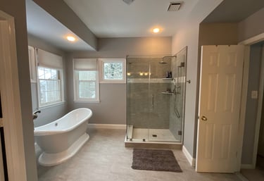 Renovated bathroom with white freestanding bathtub, stainless steel tub filler, and glass shower