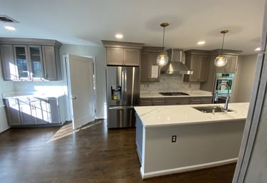 Full kitchen view: light gray cabinets, dark gray island, and brown wood flooring.
