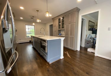 Two-tone gray kitchen remodel with dark gray island, white quartz, and brown wood floors.