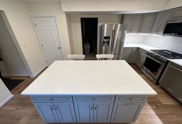 Kitchen renovation with grey pantry cabinets, stainless steel fridge, and brown LVP floors.