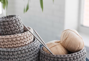 Cestas de almacenamiento hechas a mano de ganchillo en hilo gris y beige con agujas de tejer.