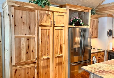 Rustic knotty pine kitchen cabinets with a stainless steel refrigerator and wood plank ceiling.