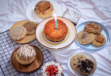Postres gourmet surtidos, incluyendo un pastel de cumpleaños con vela encendida, galletas frescas
