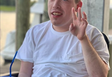 Smiling young man in a wheelchair enjoying a sunny day at an outdoor waterfront restaurant.